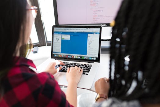 Two women working together on a laptop in a bright, modern office setting.