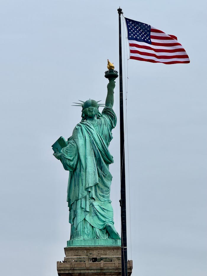 Back view of the Statue of Liberty with the American flag waving in the background.