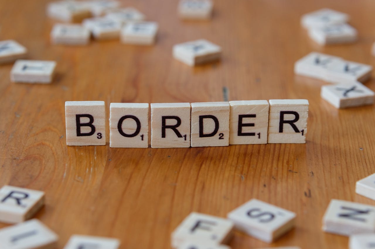 Close-up of scrabble tiles spelling 'border' against a wooden background, symbolizing boundaries.